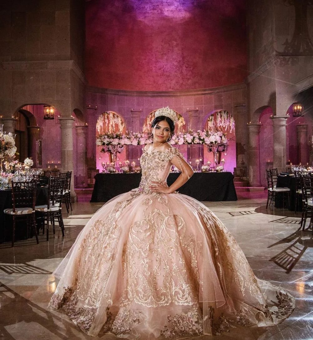 Quinceañera in a lace ball gown posing in the grand ballroom at The Bell Tower on 34th, Houston, TX, with magenta uplit arches and set reception tables.